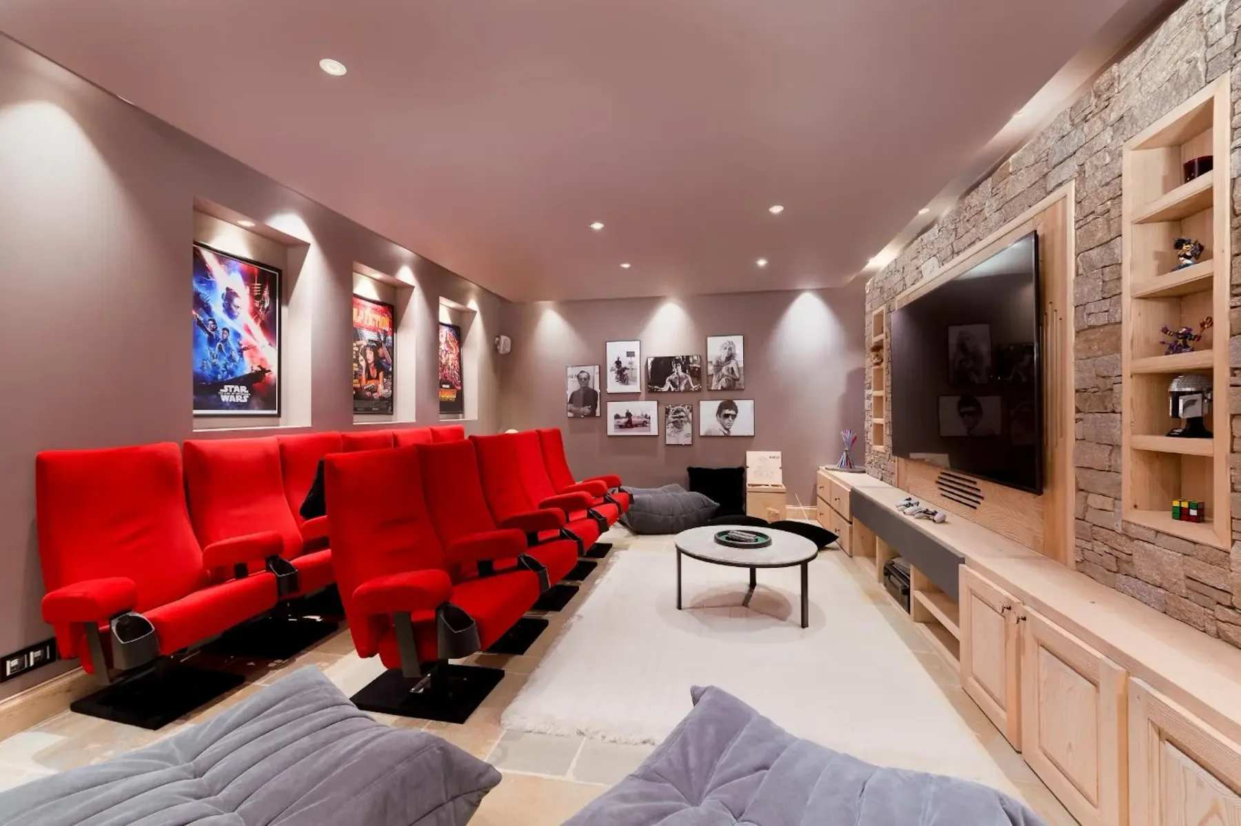 Home theater with red seats, movie posters on walls, a large screen, and cozy lighting. Beige walls and a stone accent add warmth to the room.