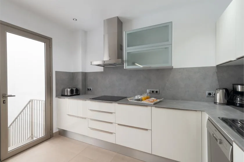 Una cocina moderna con armarios blancos, encimeras grises y una placa de cocina.