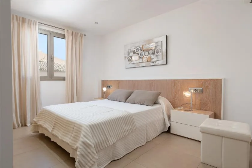 Un dormitorio luminoso con cama, mesita de noche y ventana con cortinas.