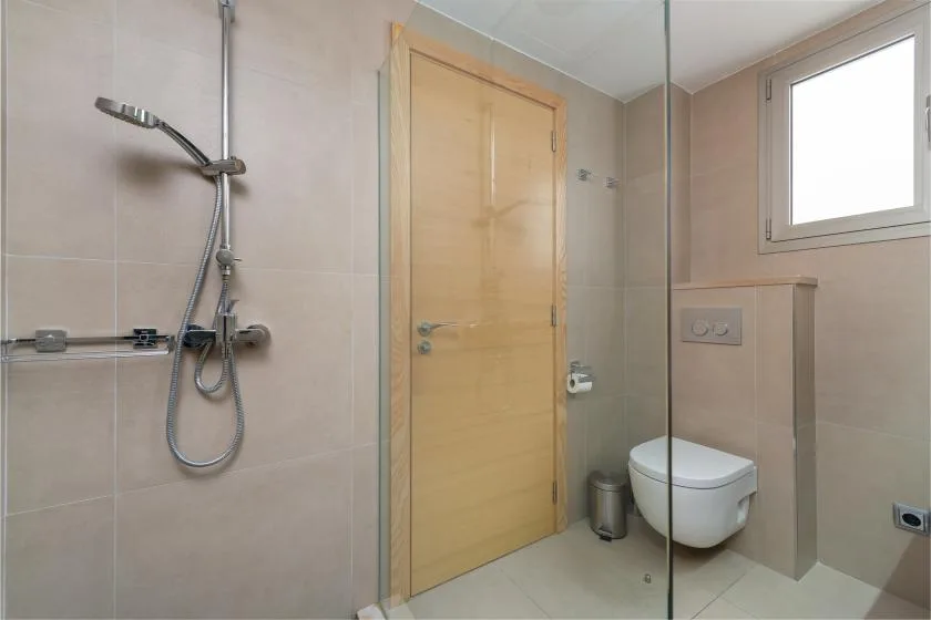 Un baño alicatado con ducha, puerta de madera e inodoro suspendido.