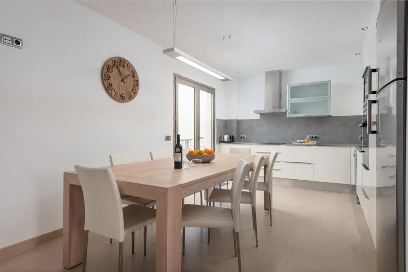 Una cocina luminosa con comedor, mesa de madera y gabinetes blancos.