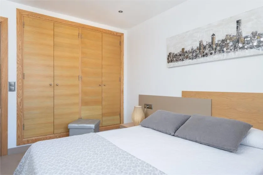 Un dormitorio con una cama, almohadas grises y armarios empotrados de madera clara.