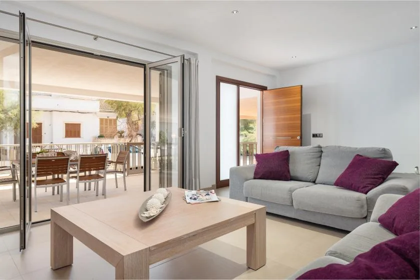 Una sala de estar con asientos grises y puertas de cristal abiertas hacia una terraza con comedor.