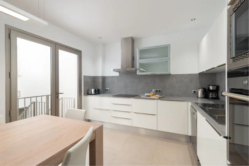 Una cocina luminosa con armarios blancos, una encimera y una mesa de comedor.