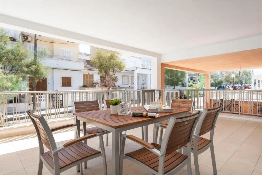 Comedor exterior cubierto con una mesa y asientos junto a una barandilla metálica.