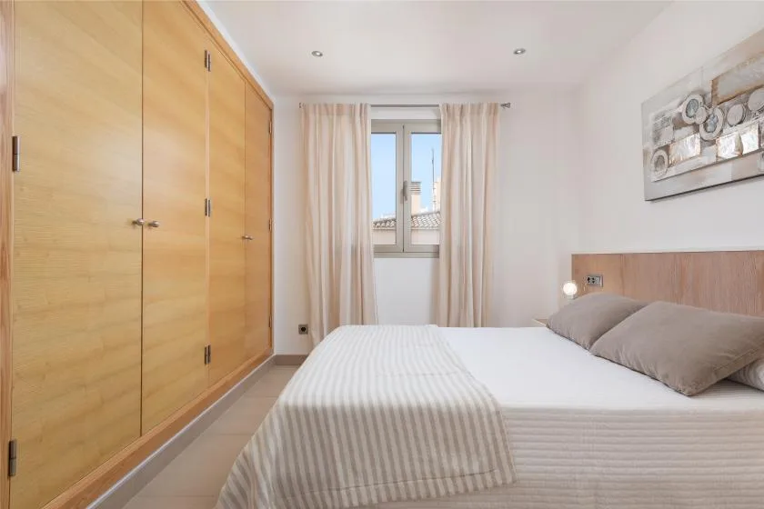 Un dormitorio luminoso con una cama, armarios de madera y una ventana con cortinas.