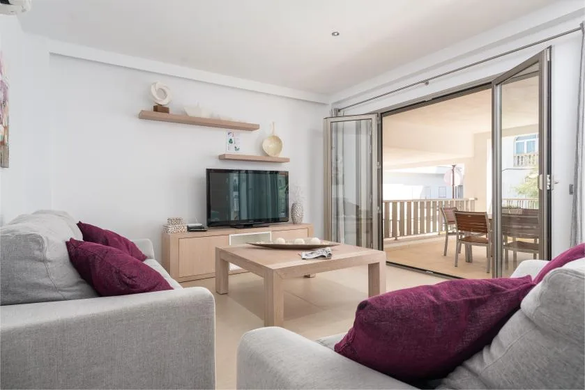 A bright living room with seating, a coffee table, and open glass doors to a balcony.