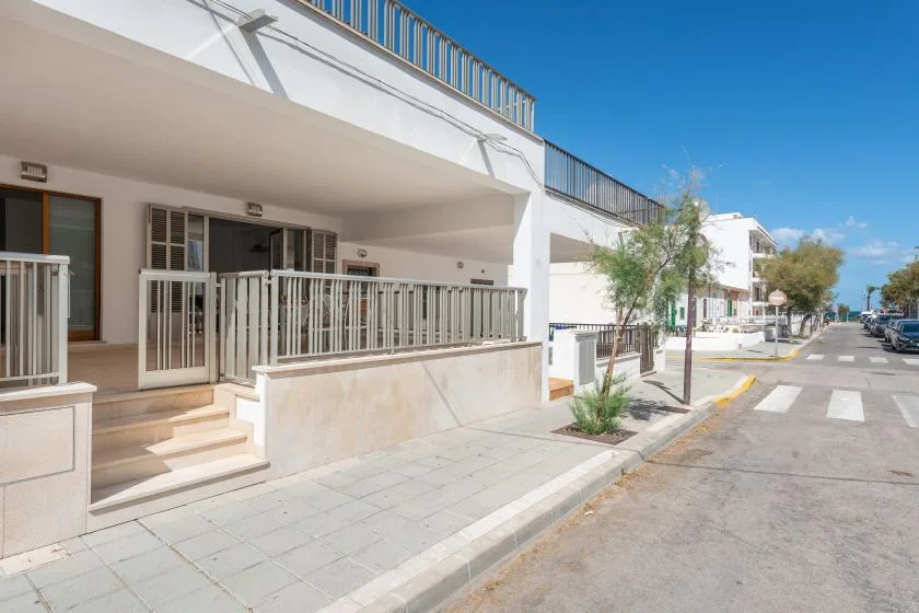 Un edificio blanco con una terraza elevada da a una calle pavimentada.