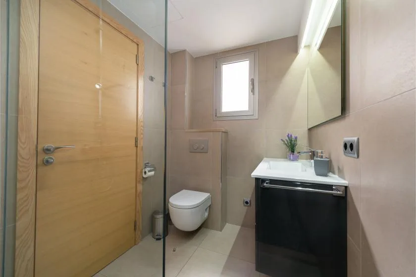 Un baño con lavabo, espejo, inodoro y puerta de madera.