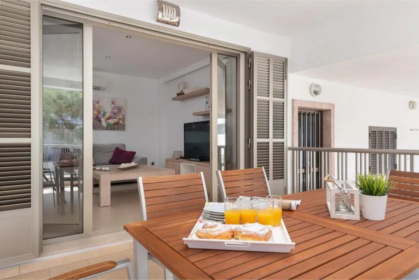 Una mesa de comedor de madera al aire libre con bebidas está junto a una puerta corredera abierta.