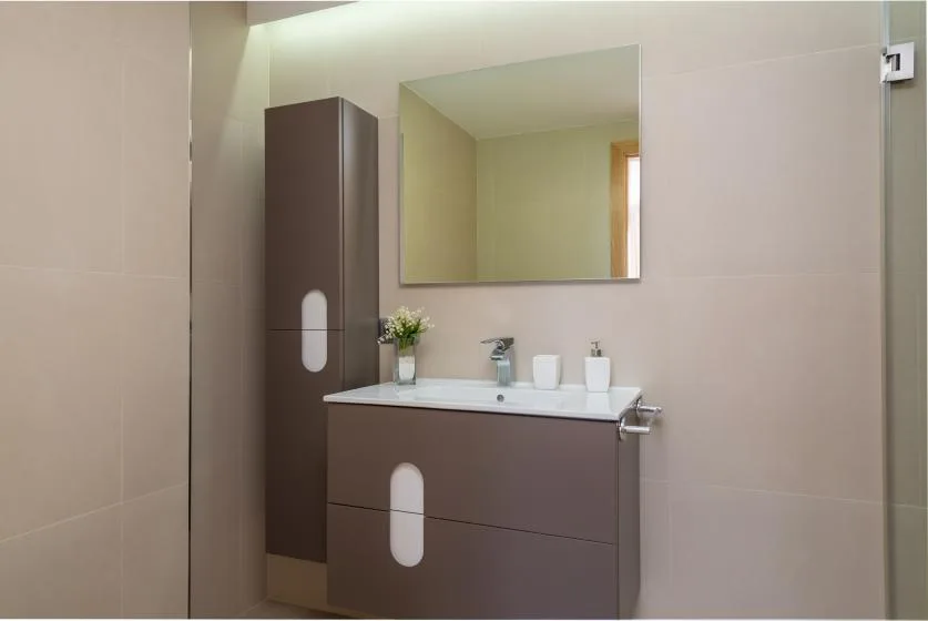 Un mueble de baño con un espejo amplio y paredes de azulejos claros.