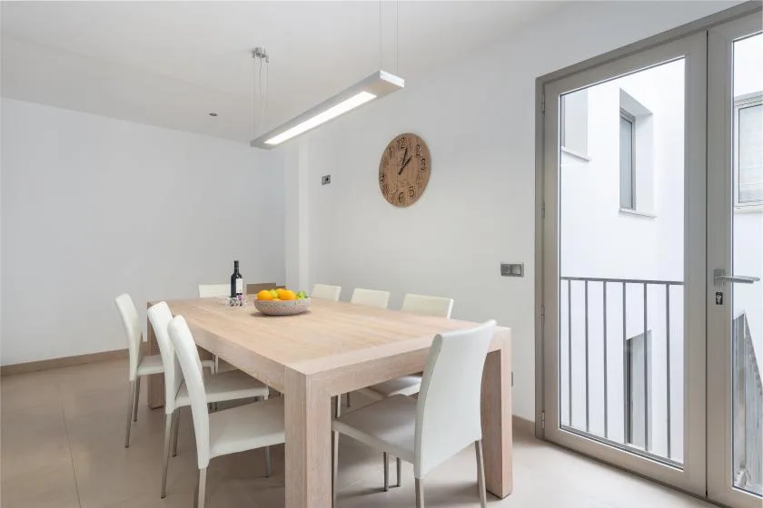 Comedor con mesa de madera, asientos blancos y una puerta grande de vidrio.