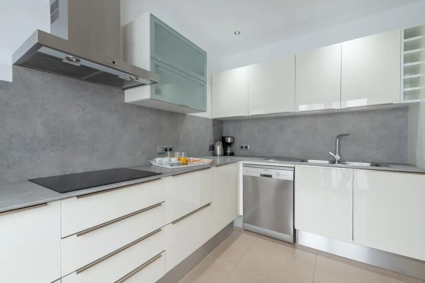 Una cocina moderna con armarios blancos, una placa de cocción oscura y un lavavajillas de acero inoxidable.