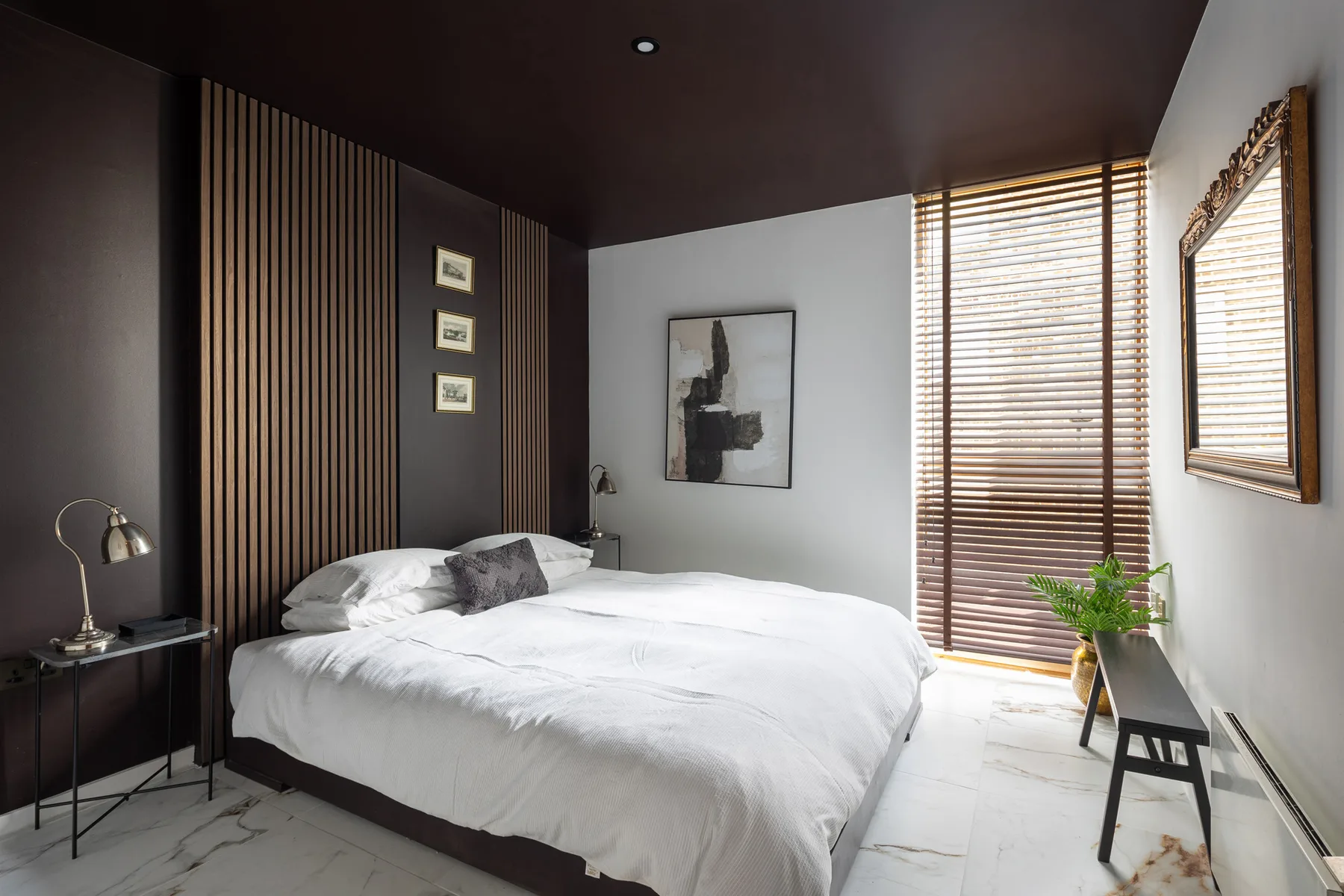 Un dormitorio con la cama tendida y persianas de madera que filtran la luz del día.