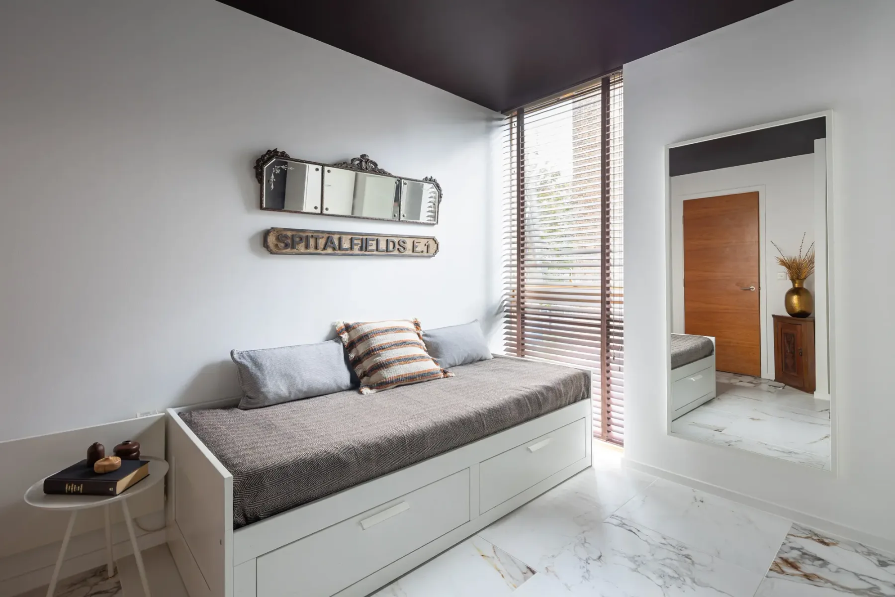 Un dormitorio luminoso con una cama de día bajo una ventana con persianas.
