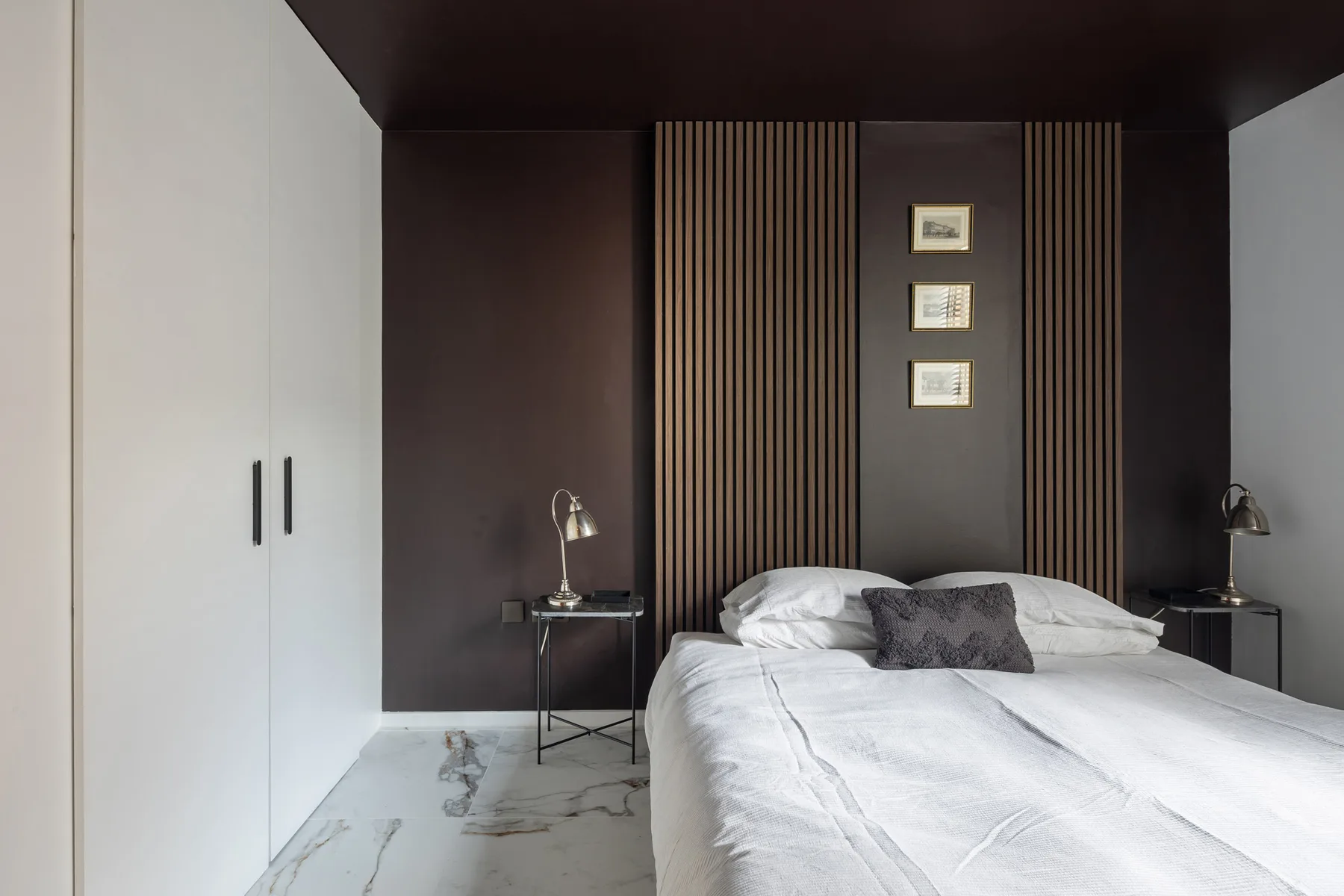 Un dormitorio con una cama, cuadros enmarcados y paneles verticales oscuros en la pared.