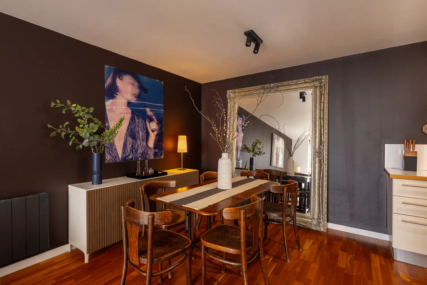 Comedor con una mesa de madera, sillas y un gran espejo enmarcado.