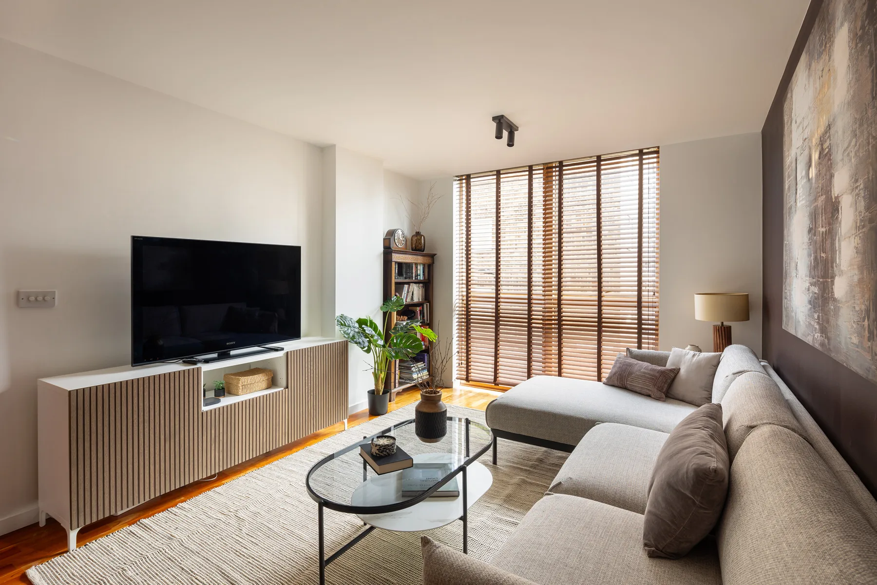 Una sala luminosa con televisión, asientos y persianas grandes en la ventana.