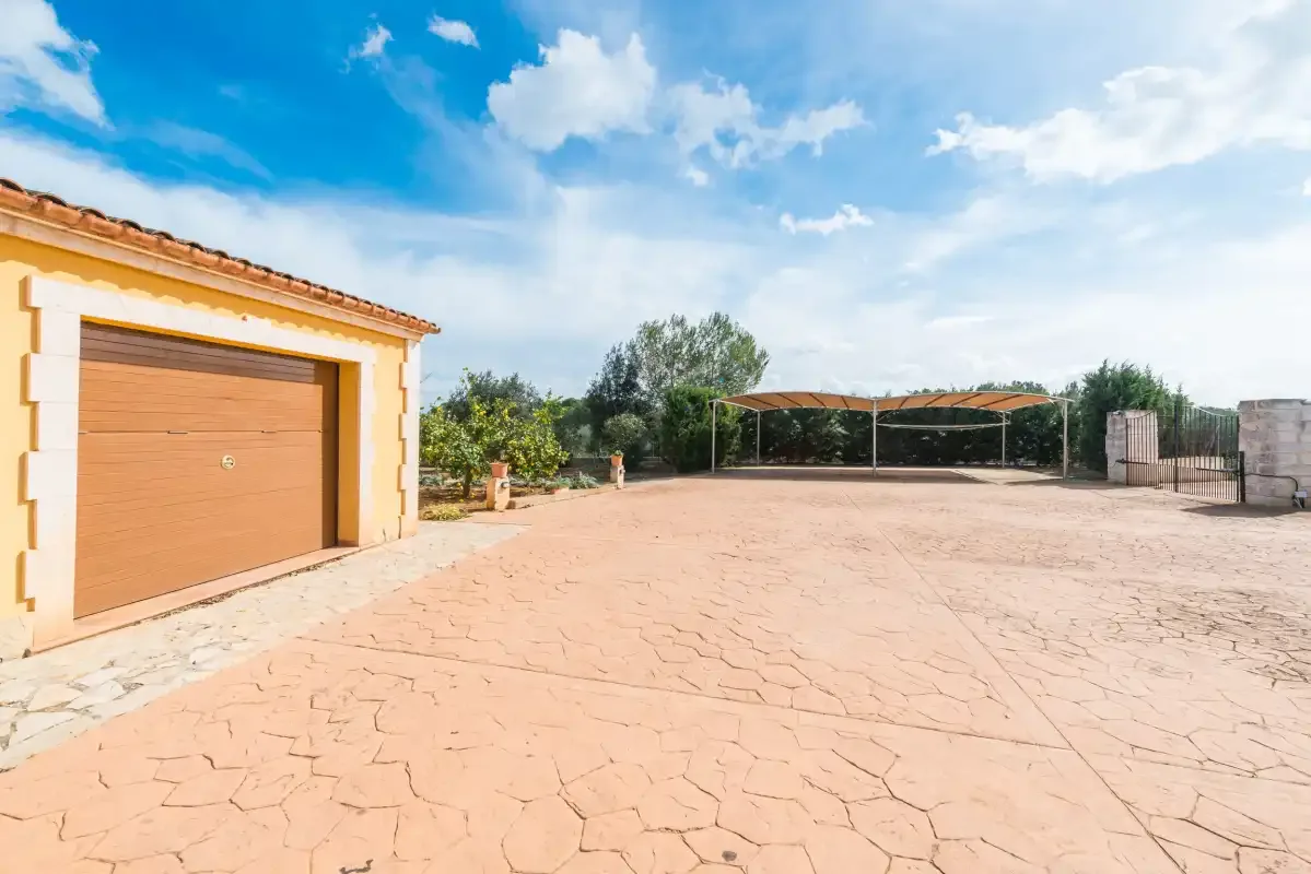 A paved outdoor courtyard sits beside a small outbuilding under a blue sky.