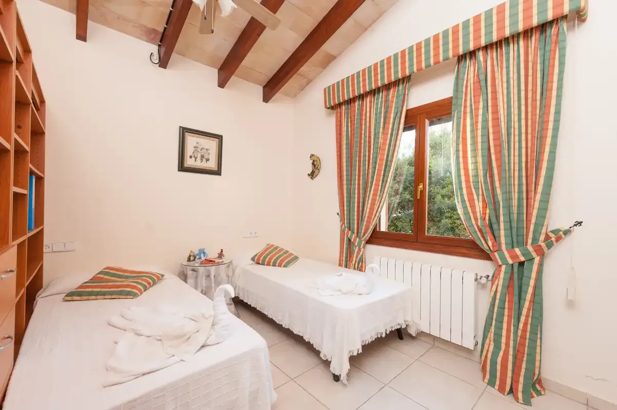 A bedroom with two single beds and striped curtains beside a window.