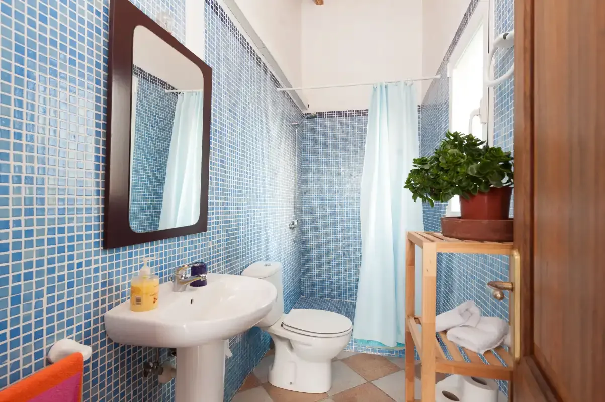 A tiled bathroom with a sink, toilet, and blue shower curtain.