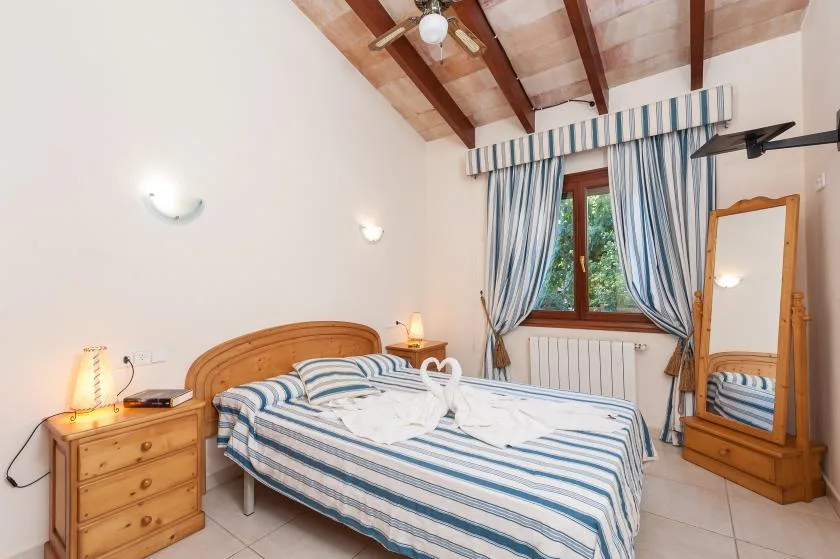 A bedroom with a striped bed, blue curtains, and exposed ceiling beams.