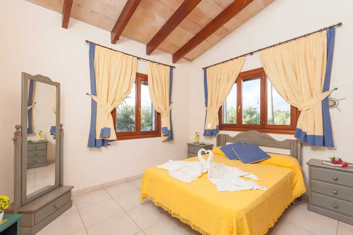 A bedroom with a yellow bedspread, blue pillows, and curtained windows.