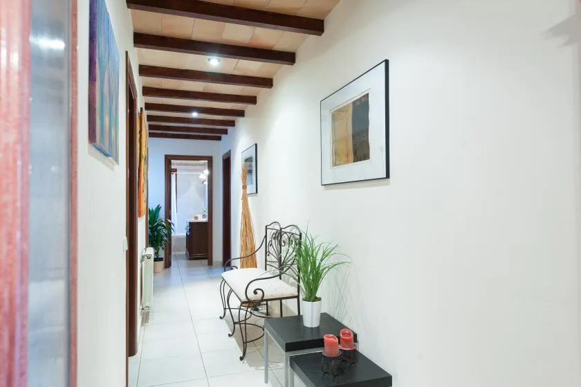 A bright hallway with framed artwork, seating, and potted plants.