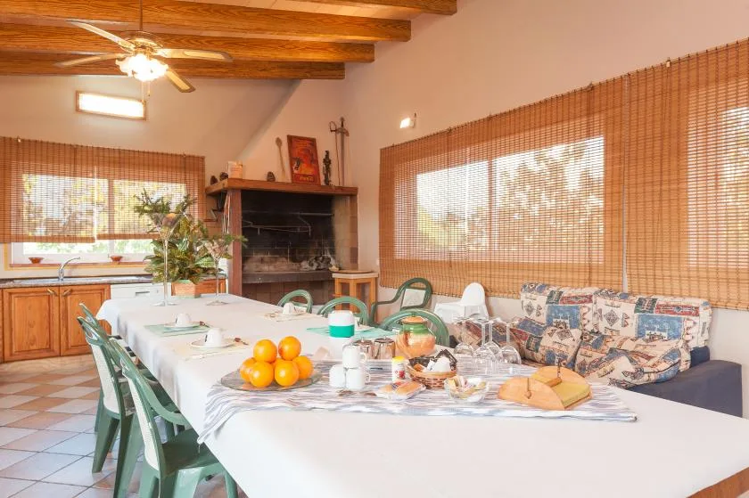 A dining area with a long table beside a fireplace and cushioned seating.