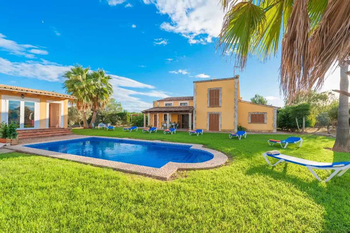A sunny villa and swimming pool sit in a green garden beneath a blue sky.
