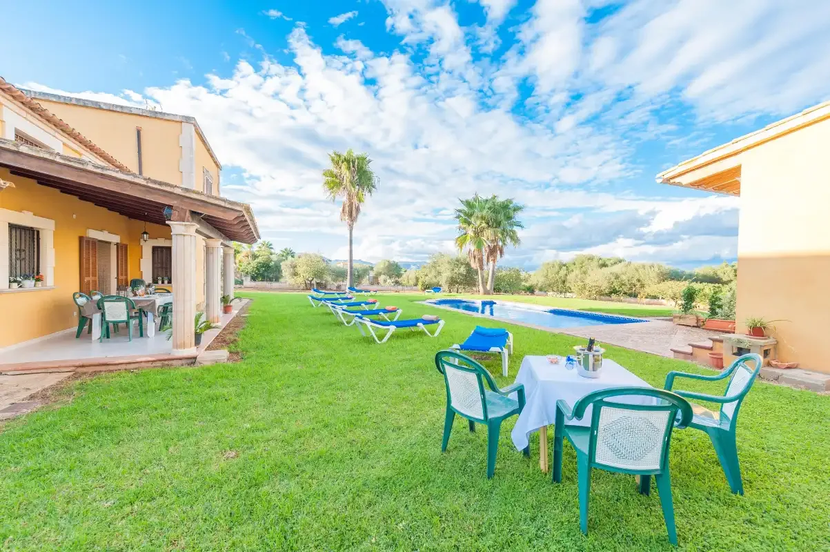 A lawn with outdoor seating overlooks a swimming pool beside a house.