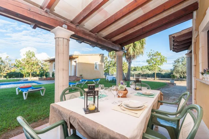 A covered outdoor dining area with a set table overlooking a garden.