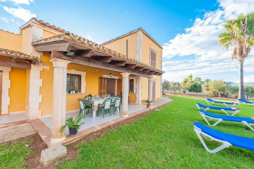A sunny garden patio with outdoor dining seating and blue loungers on the lawn.