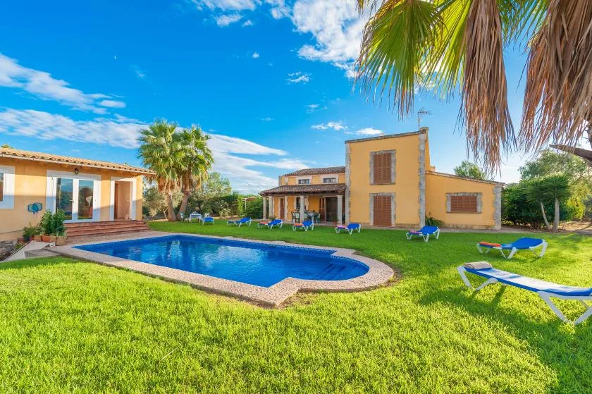 A swimming pool and lawn sit in front of a house under a bright blue sky.