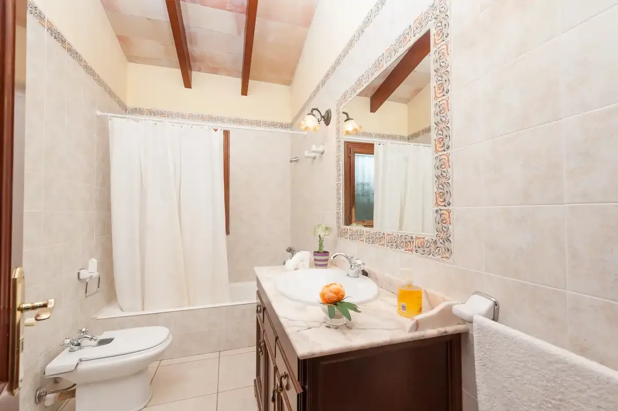 A tiled bathroom with a sink, mirror, and curtained shower area.