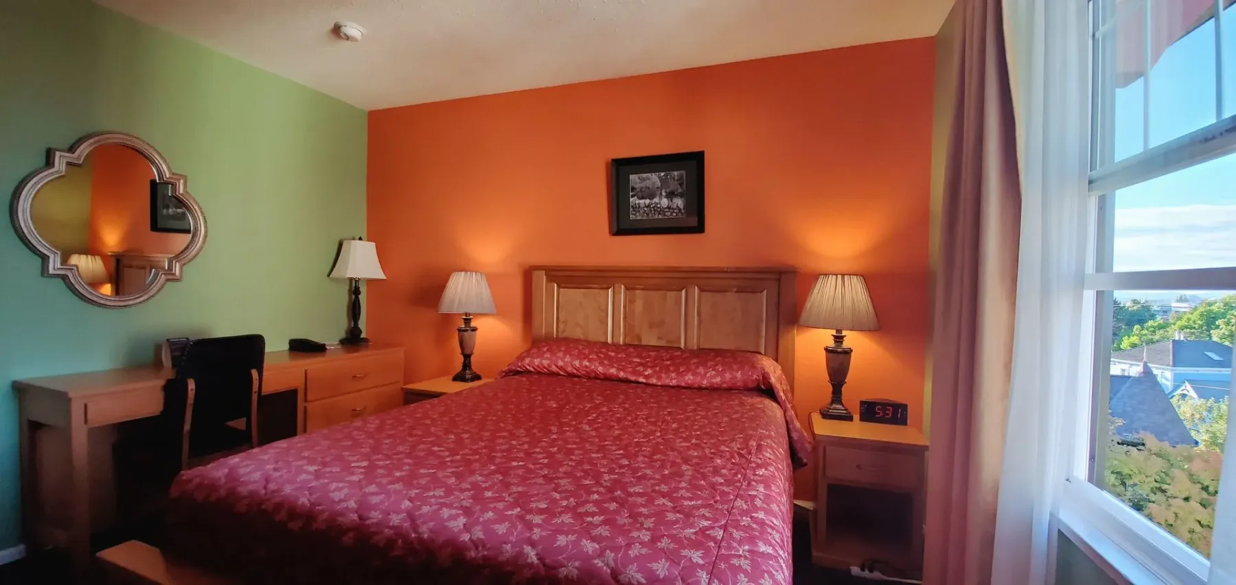 Una habitación de hotel con una cama, lámparas, un espejo y una ventana