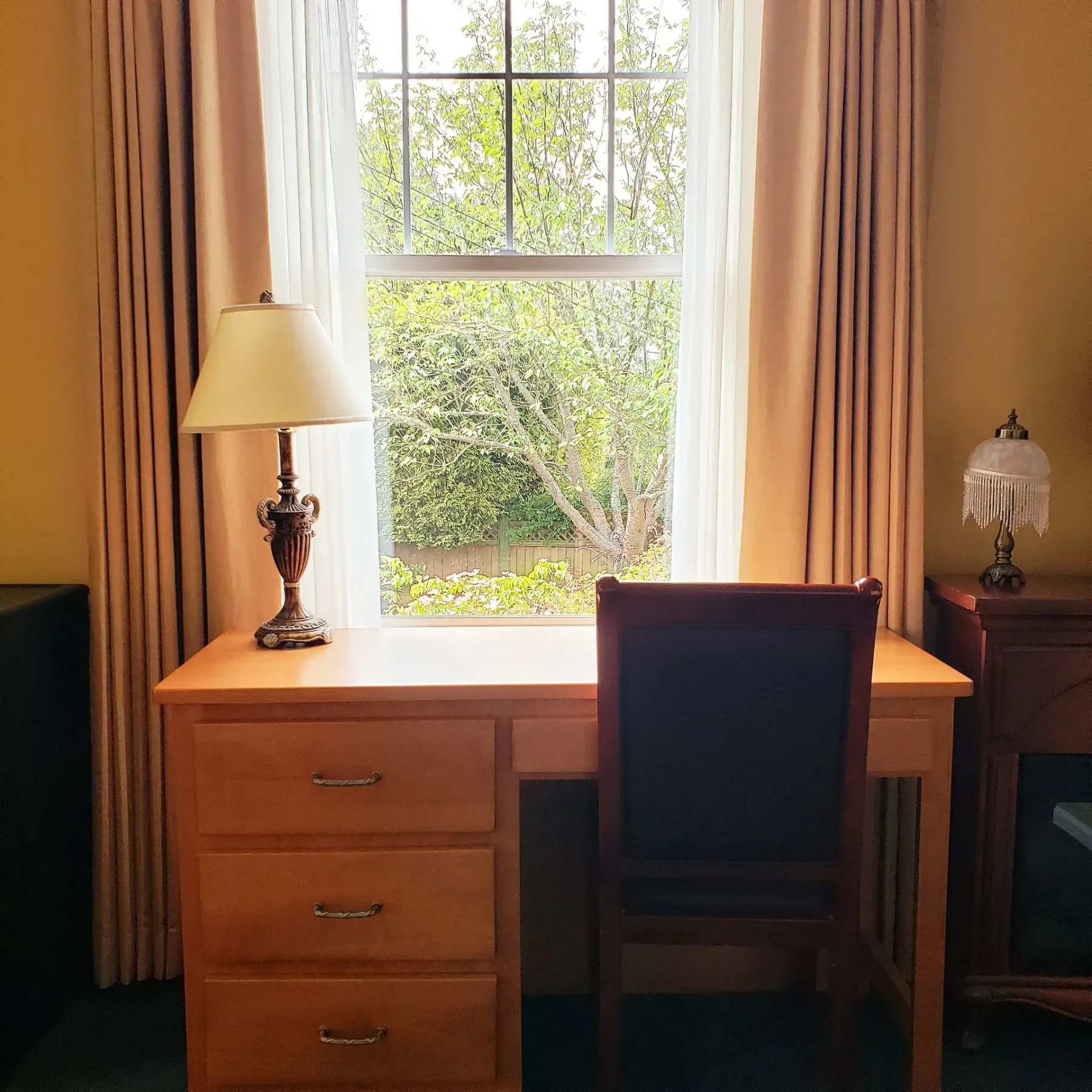 Un escritorio, una lámpara y una silla frente a una ventana
