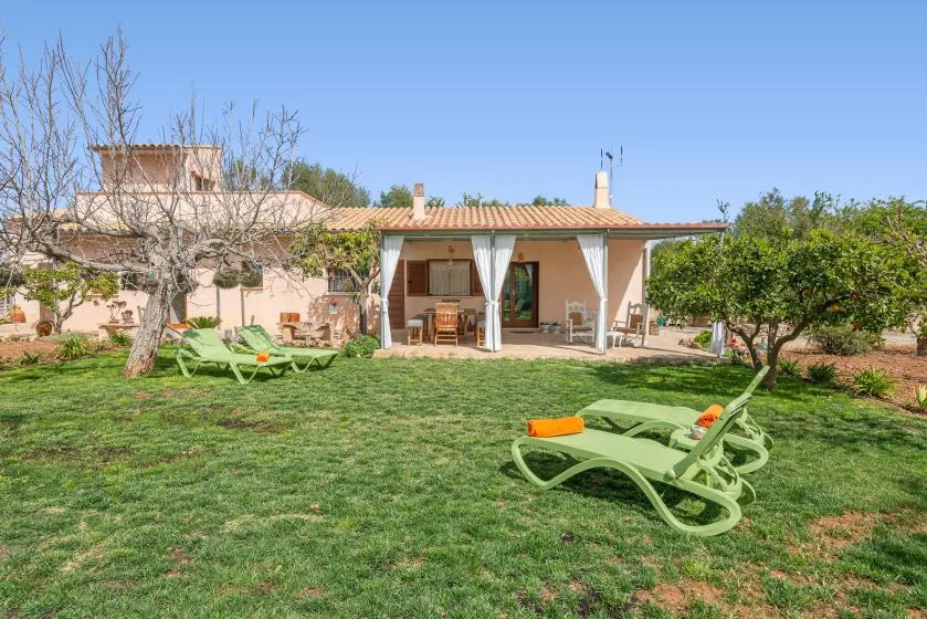Una casa se abre a un jardín con césped, asientos y tumbonas.