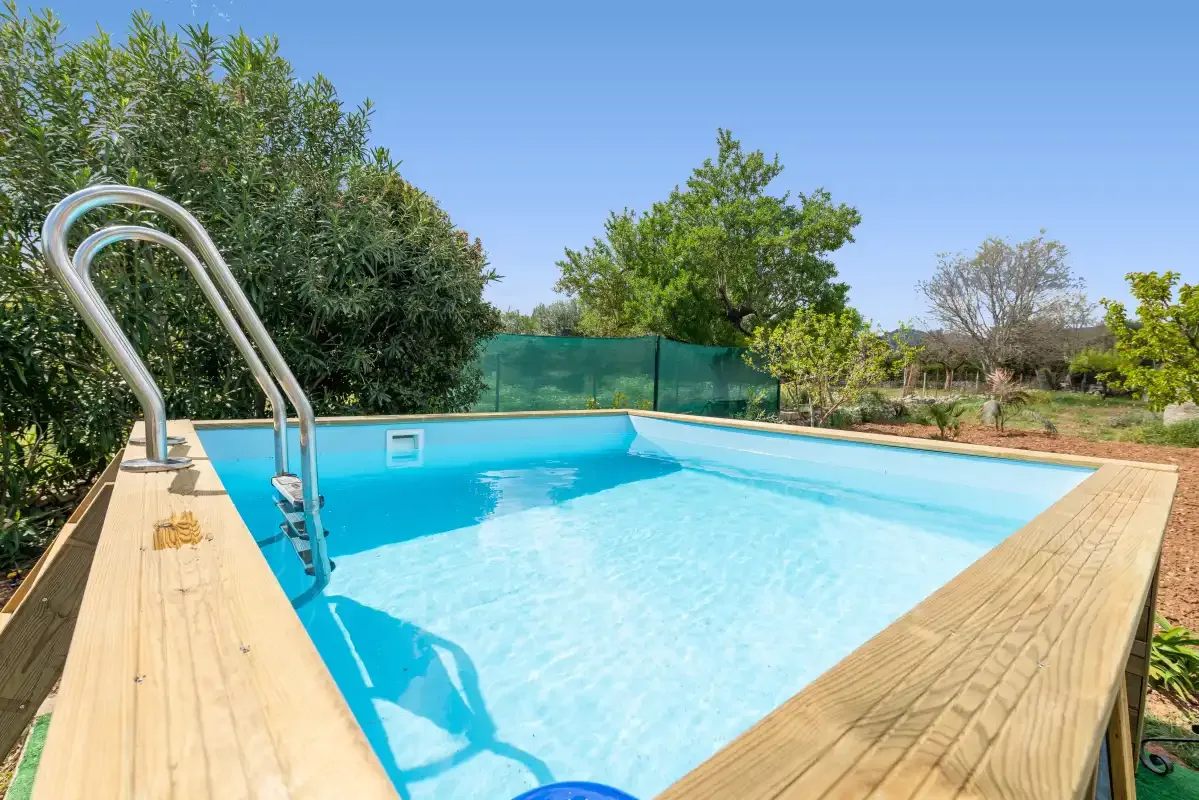 Una piscina al aire libre con una tarima de madera y árboles alrededor.