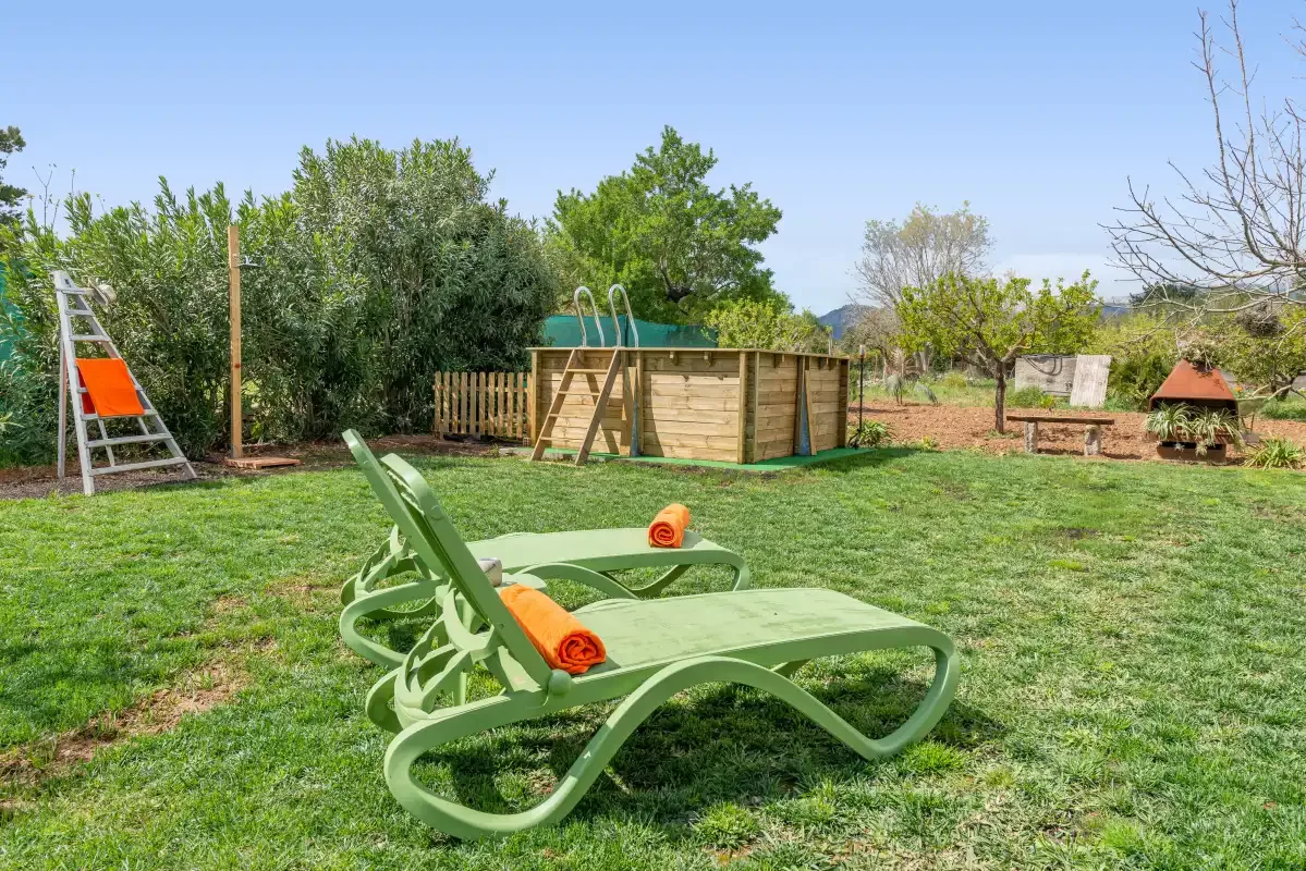 Un jardín con césped, tumbonas reclinables y una pequeña piscina elevada.