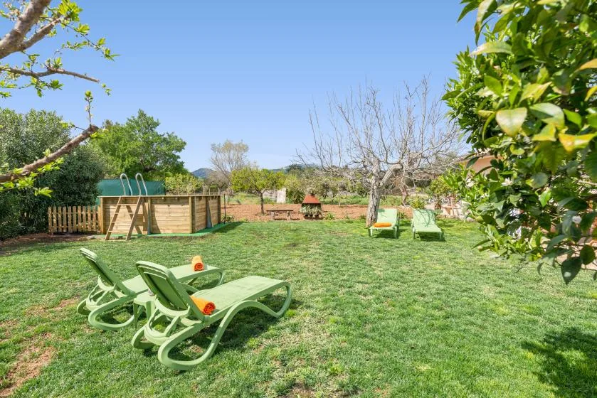 Un jardín con césped, tumbonas verdes, árboles y una estructura de juego de madera.