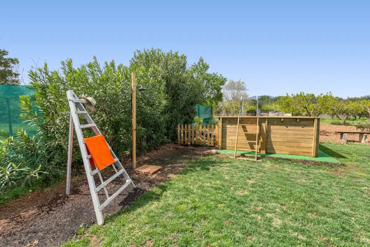 Un jardín con césped, una valla de madera y una escalera junto a arbustos frondosos.