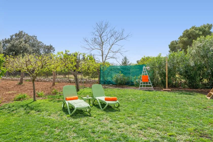 Un jardín con césped, dos sillones reclinables y árboles al fondo.