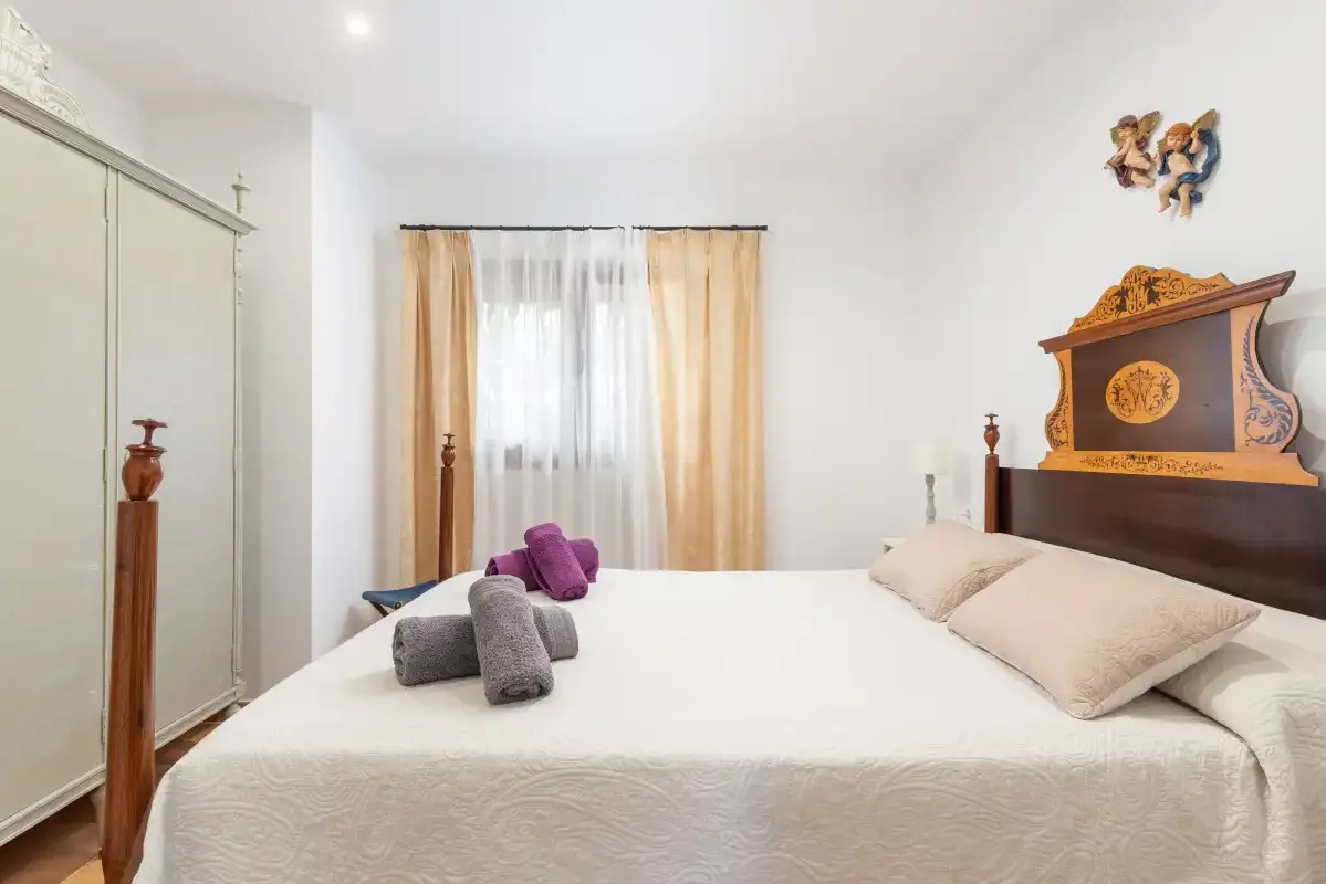Un dormitorio con una cama bajo una ventana con cortinas transparentes.