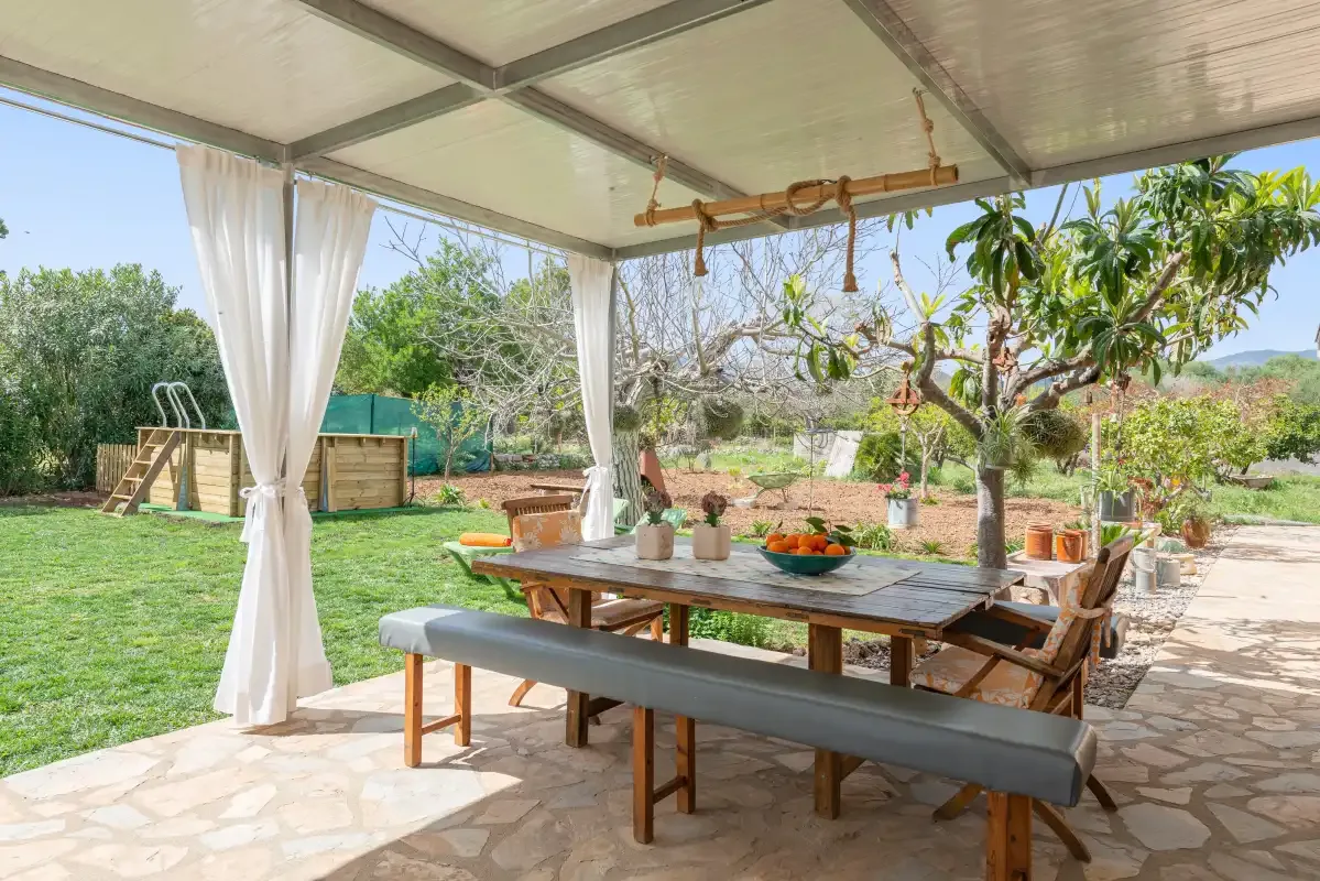 Una zona de comedor exterior a la sombra con una mesa de madera y vistas al jardín.