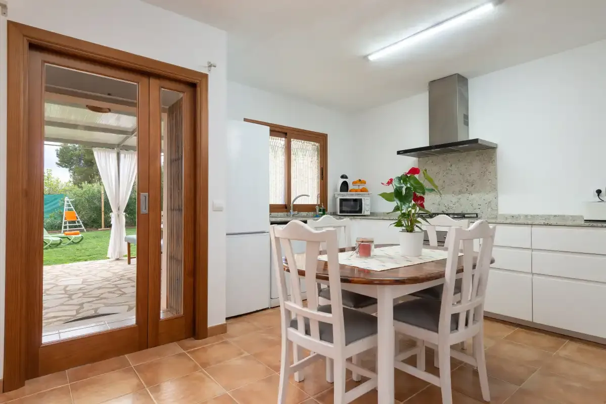Cocina y comedor con una mesa junto a una puerta de cristal que da al jardín.
