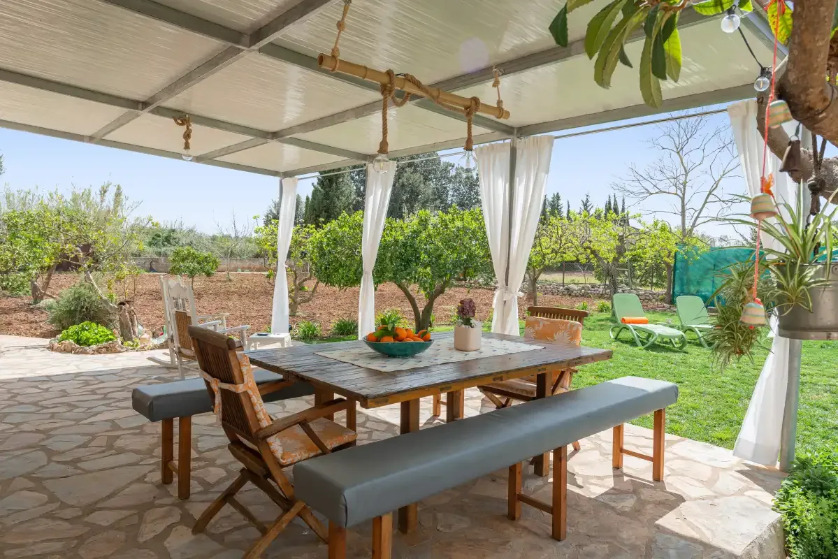 Una zona de comedor exterior cubierta con mesa y asientos da a un jardín.