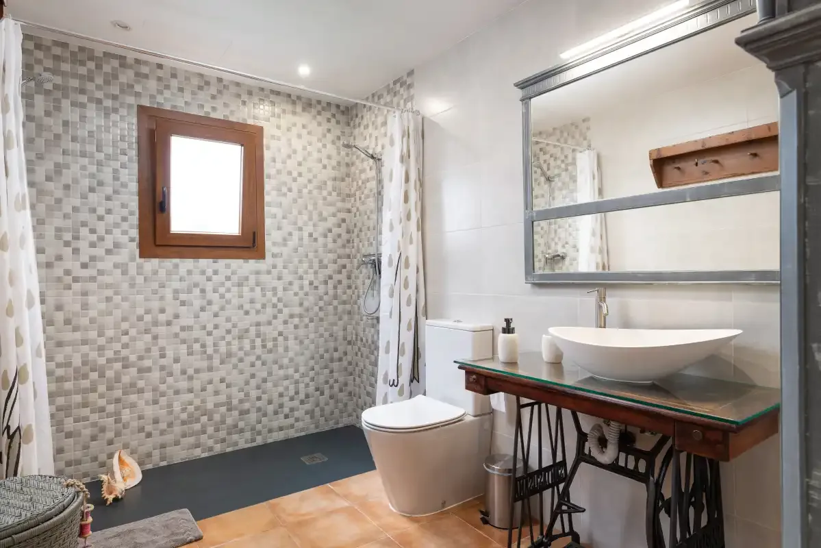 Un baño alicatado con ducha, inodoro y lavabo sobre encimera.