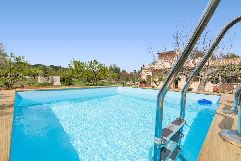 Una piscina al aire libre con una barandilla metálica y árboles al fondo.