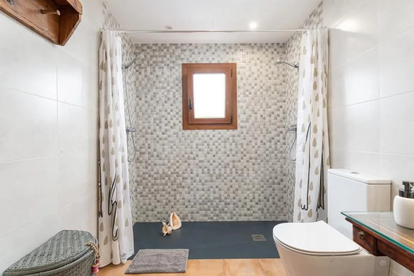Baño con zona de ducha alicatada, cortinas estampadas y una ventana pequeña.